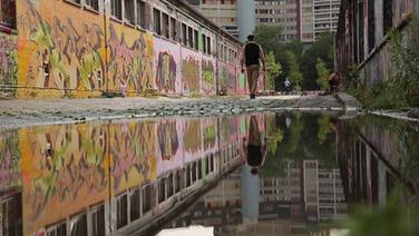 Ein Mann geht an einer Wand mit Graffitis vorbei. © NDR 