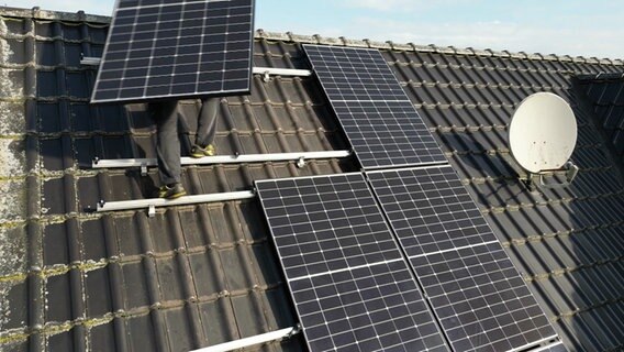 Eine Person bringt Solarmodule auf einem Dach an. © NDR 