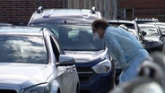 Ein Arzt mit Schutzmaske steht seitlich an einem Auto © NDR Foto: Screenshot
