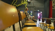 Eine Frau sitzt auf einem Stuhl in einer, um sie herum sind alle Stühle leer © NDR Foto: Screenshot