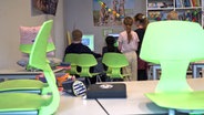 Kinder stehen vor Computern, im Vordergrund aufgestellte grüne Stühle in einem Klassenzimmer © NDR Foto: Screenshot