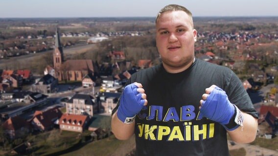 Thumbnail: Ein Mann mit Boxhandschuhen und einem ukrainischen T-Shirt, im Hintergrund die niedersäschsische Gemeinde Molbergen. © NDR Foto: screenshot