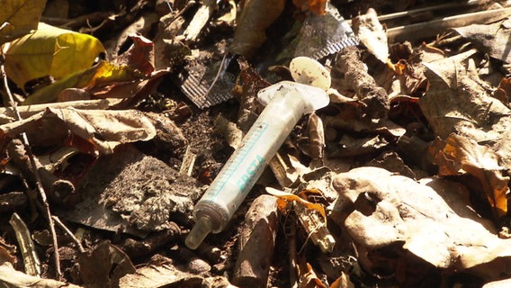 Eine Drogenspritze liegt zwischen Laub auf dem Boden © NDR 