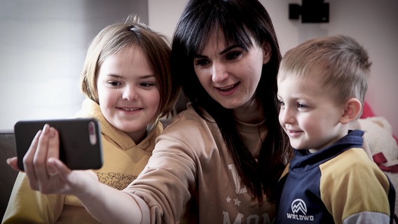 Die Ukrainerin Natascha, ihre Tochter Varja und ihr Sohn Bogdan schauen in ein Smartphone. © NDR 