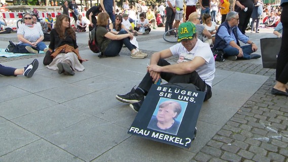 Demonstrant gegen die Corona-Maßnahmen in Hamburg mit Plakat gegen Angela Merkel © NDR Foto: Screenshot