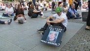 Demonstrant gegen die Corona-Maßnahmen in Hamburg mit Plakat gegen Angela Merkel © NDR Foto: Screenshot
