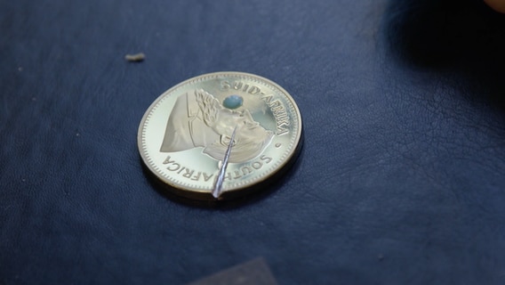 Eine vermeintliche Goldmünze liegt auf einem blauen Untergrund © NDR Foto: Screenshot