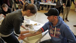 Eine Frau nimmt eine Blutprobe bei einem jungen Mann im Rahmen einer Typisierungsaktion. © NDR