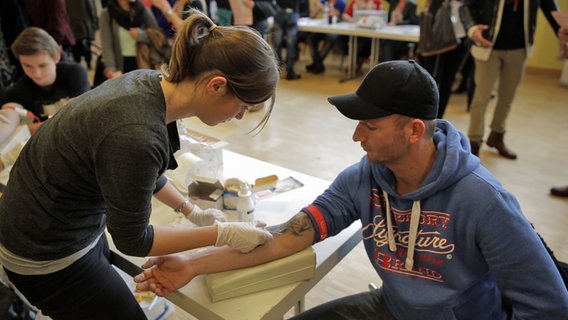 Eine Frau nimmt eine Blutprobe bei einem jungen Mann im Rahmen einer Typisierungsaktion. © NDR 