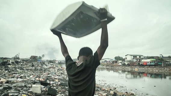 Ein Mann schleudert einen kaputten Fernseher auf einer Müllkippe in Ghana zu Boden. © NDR/ARD 