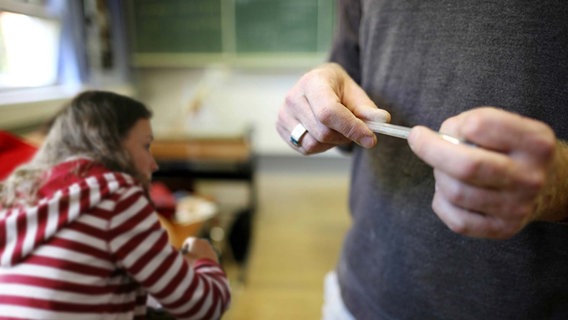 Der Lehrer geht mit einem Stift in der Hand durch den Klassenraum. © imago/Gerhard Leber, imago/McPHOTO Foto: Gerhard Leber
