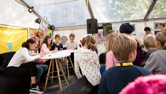 Emma Roth, Emilia Flint, Marleen Quentin, Luke Matt Röntgen und Ruben Storck sitzen an einem Tisch auf der Bühne vor ihren Fans und unterschreiben Autogrammkarten. © NDR Foto: Claudia Timmann