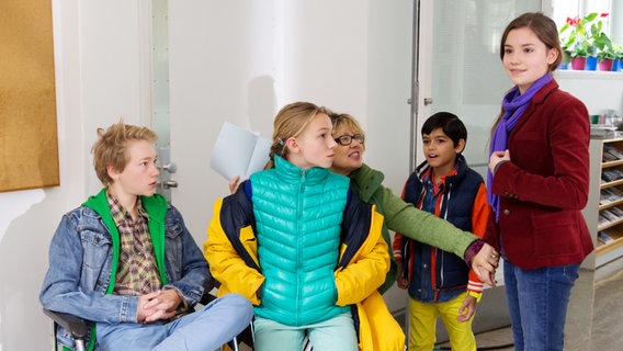 Max, Jessi, und eine Frau sitzen vor Luis und Nina in einem Flur. © NDR Foto: Claudia Timmann