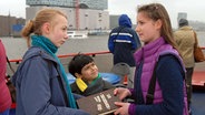 Nina (Carolin Garnier, rechts) übergibt Jessi (Martha Fries, links) und Luis (Emilio Sanmarino, Mitte) das Pfefferkörnerbuch. © NDR/Studio HH Foto: Romano Ruhnau