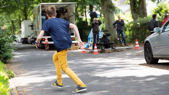Niklas (Jaden Dreier) läuft geduckt über die Straße. Im Hintergrund sieht man das Kamerateam. © NDR Foto: Claudia Timmann