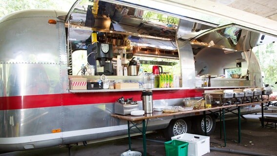 Ein aufgebautes Catering steht vor einem silbernen Wohnwagen. © NDR Foto: Claudia Timmann