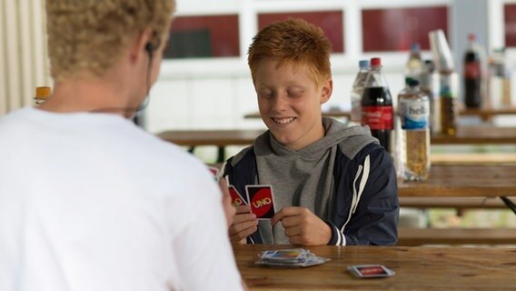 Timo Glinka sitzt am Tisch und hält Spielkarten in der Hand. © NDR Foto: Claudia Timmann