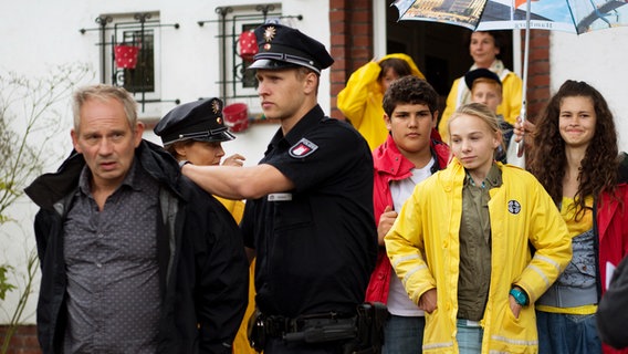 Stucke (Michael Lott) wird von einem Polizisten abgeführt. Im Hintergrund stehen die Pfefferkörner Anton (Danilo Kamber), Ceyda (Merle de Villiers) und Jessi (Martha Fries). © NDR Foto: Claudia Timmann