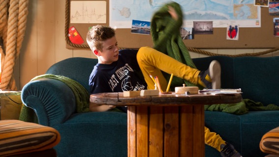Niklas (Jaden Dreier) schlägt die Decke zurück um vom Sofa aufzustehen. © NDR Foto: Claudia Timmann