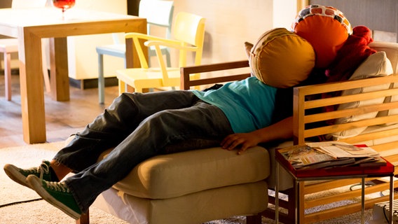 Danilo Kamber liegt mit zwei Kissen auf dem Gesicht auf einem Sofa. © NDR Foto: Claudia Timmann