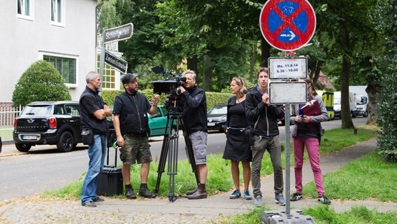 Ein Kameramann und vier Drehteammitarbeiter stehen mit einer Filmkamera auf einem Stativ an einer Straße. Rechts steht ein Halteverbotsschild. © NDR Foto: Claudia Timmann