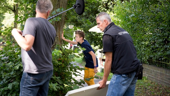 Niklas (Jaden Dreier) steht versteckt hinter einem Baum und lugt durch die Blätter. © NDR Foto: Claudia Timmann