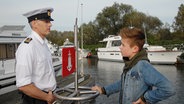 Niklas (Jaden Dreier) im Gespräch mit dem Wasserschutzpolizisten (Roland Kieber, links). © NDR/Studio HH Foto: Romano Ruhnau