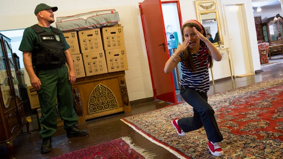 Ava Sophie macht eine Karatefigur vor einem Komparsen in Zollbeamten-Uniform. © NDR Foto: Claudia Timmann