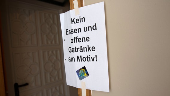 Ein Zettel mit der Aufschrift "Kein Essen und offene Getränke am Motiv" klebt am Türrahmen. © NDR Foto: Claudia Timmann