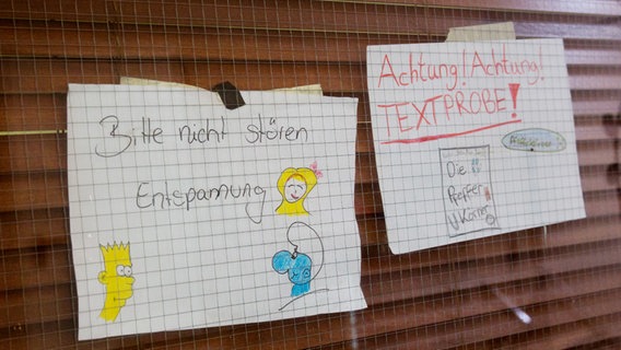 Zwei Zettel mit der Aufschrift " Bitte nicht stören - Entspannung" und "Achtung Textprobe" kleben vor einem Fenster. © NDR Foto: Claudia Timmann