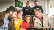 Jale (Ava Sophie Richter, Mitte) schaut mit Polizisten und dem Ehepaar Kelmendi (Kida Ramadan, Neshe Demir, links) auf ein Notebook. © NDR/Studio HH Foto: Boris Laewen