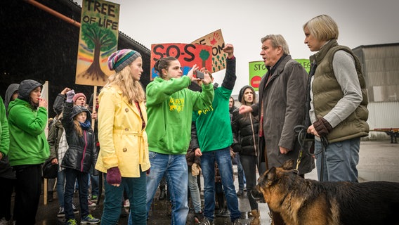 Stella (Zoë Malia Moon, links vorne) demonstriert mit einer Gruppe junger Leute vor Holzhändler Adam Linde (Michael Kind, 2. von rechts) und dessen Tochter Evelyn (Sandra Maren Schneider, rechts). © NDR/Studio HH Foto: Boris Laewen