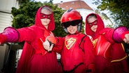Stella (Zoë Malia Moon, links), der Rote Blitz (Lilly Barshy, Mitte) und Pinja (Sina Michel) in roten Superhelden-Kostümen. © NDR/Studio HH Foto: Boris Laewen