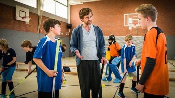 Ramin (Jann Piet, links) und Tom (Vincent Grages) stehen mit Hockeytrainer John (Andreas Nickl) in der Halle. © NDR/Studio HH Foto: Boris Laewen