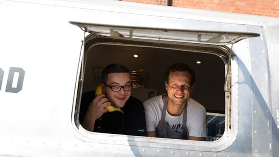 Zwei Cateringmitarbeiter schauen aus einem Caravanfenster. © NDR Foto: Claudia Timmann