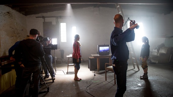 Filmteammitarbeiter und Schauspieler stehen in einem staubigen und dunklen Raum. © NDR Foto: Claudia Timmann