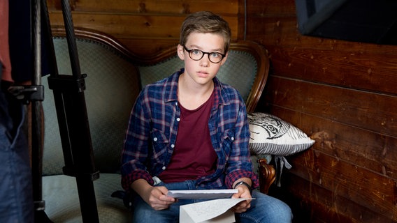 Benny (Ruben Storck) sitzt auf einem Sofa und hält einen Brief in der Hand. © NDR Foto: Claudia Timmann