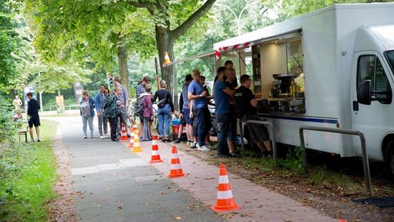 Ein Cateringwagen steht an der Straße, davor steht eine Reihe an Menschen. © NDR Foto: Claudia Timmann