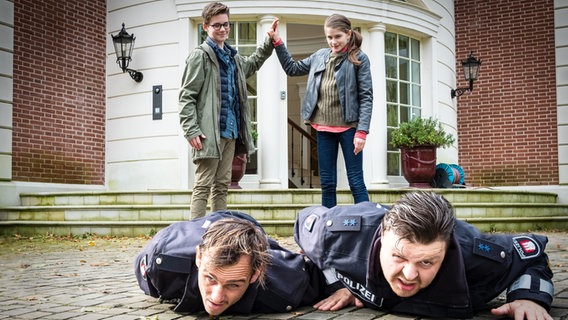 Benny (Ruben Storck, hinten links) und Mia (Marleen Quentin) stehen hinter zwei Männern (Peter Sikorski, Marius Borghoff), die am Boden liegen. © NDR/Studio HH Foto: Boris Laewen