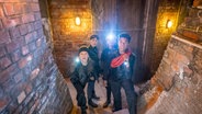 Kira, Nele, Levin und Tayo sind mit Taschenlampen in einem Kellergewölbe unterwegs © NDR Foto: Boris Laewen