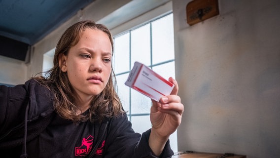 Kira (Marlene von Appen) hält eine Packung mit Dopingmittel in der Hand und schaut nachdenklich. © NDR Foto: Boris Laewen