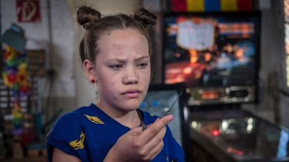 Kira (Marlene von Appen) hält etwas in der Hand und schaut skeptisch. © NDR Foto: Boris Laewen
