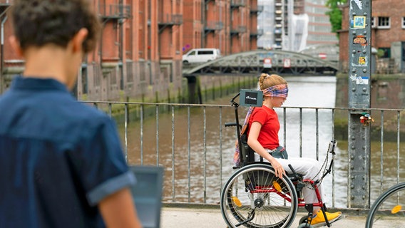 Pippa fährt mit verbundenen Augen im Rollstuhl, Tarun steht mit dem Laptop dabei. © NDR/Letterbox Foto: Boris Laewen