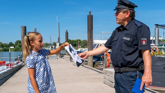 Clarissa überreicht dem Polizisten ein Bild, auf dem das Gesicht eines Mannes zu erkennen ist. © NDR/Letterbox Foto: Boris Laewen