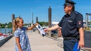 Clarissa überreicht dem Polizisten ein Bild, auf dem das Gesicht eines Mannes zu erkennen ist. © NDR/Letterbox Foto: Boris Laewen