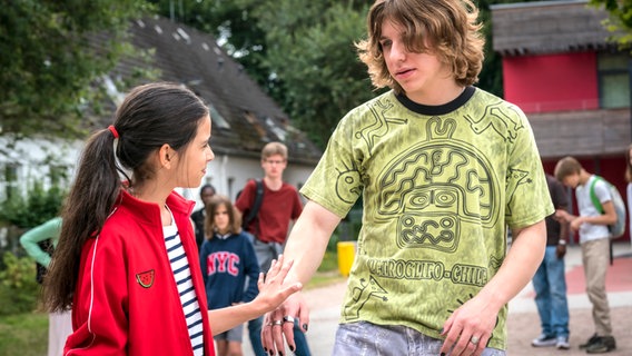 Jasina macht auf dem Schulhof eine abwehrende Handbewegung ihn Richtung eines Mitschülers. © NDR/Letterbox Foto: Boris Laewen