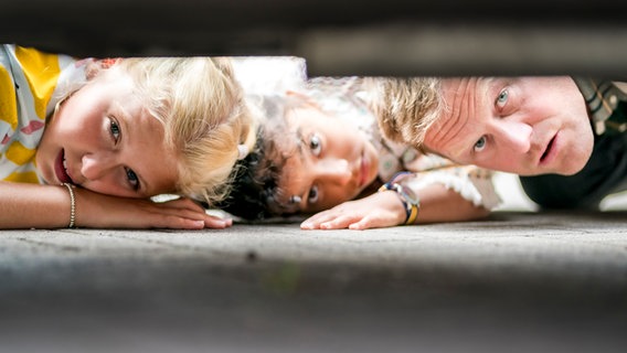 Nika (Lavinia Burat), Amy und Lars (Tim Ehlert) schauen unter das Auto und stellen fest, dass der Katalysator weg ist. © NDR/Letterbox Foto: Boris Laewen