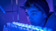 Hakim ist in einem Labor mit blauen Licht. © NDR/ Letterbox Foto: Boris Laewen