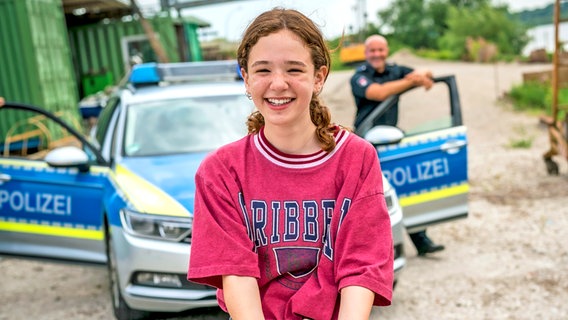 Leo steht lachend vor einem Polizeiwagen. © NDR/Letterbox Foto: Boris Laewen