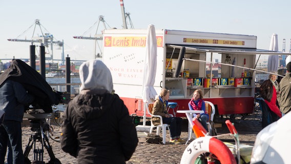 Kamera und Mikro sind auf Max und Tatja gerichtet, die an einem Tisch am Hafen vor Lenis Imbiss sitzen. © NDR Foto: Claudia Timmann